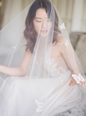 A bride wearing a blusher wedding veil adorned with lace butterflies. 